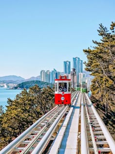 a red and white train traveling over a bridge next to the ocean with tall buildings in the background