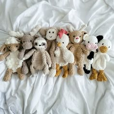 a group of stuffed animals laying on top of a white bed covered in sheets and pillows