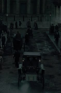 an old car driving down a street at night with people standing around and riding in the back