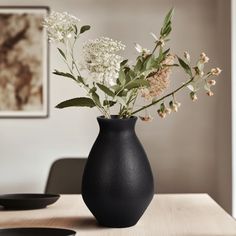 a black vase filled with white flowers on top of a wooden table next to plates