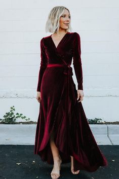 a woman wearing a red velvet dress and heels standing in front of a white wall