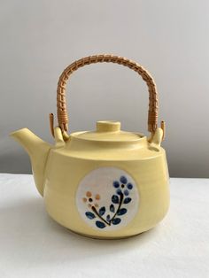 a tea pot with a handle decorated with blue and yellow flowers on the outside, sitting on a white surface