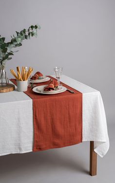 the table is set with two plates and silverware on it, along with an orange linen runner