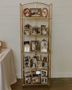 a gold shelving unit with pictures and photos on the shelves, next to a white table cloth