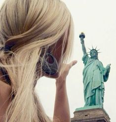 a woman with headphones on looking at the statue of liberty in new york city