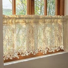 a window with lace curtains hanging on it's side in front of a window sill