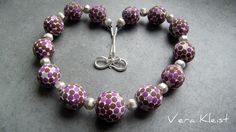 a purple and white beaded bracelet with silver beads on a gray surface, in the shape of a heart