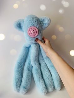 a blue teddy bear with a pink button on it's face is being held by someone