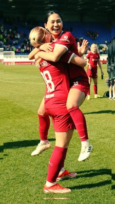 two women in red soccer uniforms are hugging each other on the field with their arms around one another