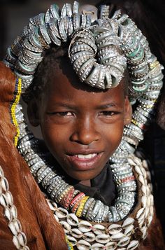 a young boy with many rings on his head and necklaces around his neck, smiling for the camera