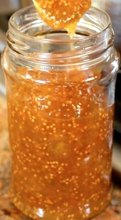 a spoon full of honey sitting on top of a glass jar filled with orange liquid