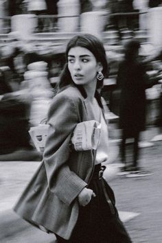 a woman walking down the street while wearing a coat and holding a cup in her hand