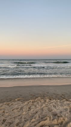 a surfboard sitting on top of a sandy beach next to the ocean at sunset