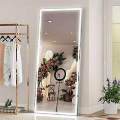 a large mirror in the middle of a room with clothes hanging on racks and flowers