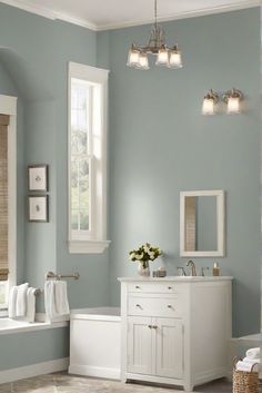 a bathroom with blue walls and white furniture in the corner, along with two windows