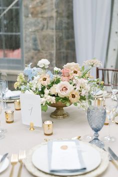 an elegant centerpiece is displayed on a table with silverware and gold place settings