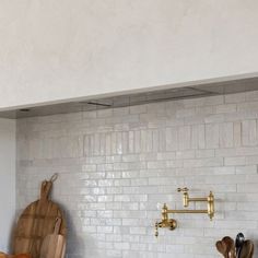 a kitchen with white brick walls and wooden utensils hanging on the wall next to a cutting board