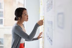 a woman standing in front of a whiteboard with headphones on and writing on it