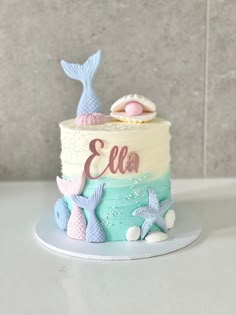 a little mermaid themed birthday cake on a plate with shells and seashells around it