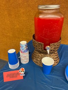 a blue table topped with cups and a jar filled with liquid