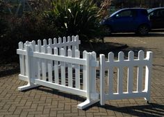 a white picket fence sitting on the side of a road next to a blue car