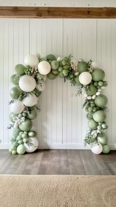 an arch made out of balloons and greenery on the floor in front of a white wall