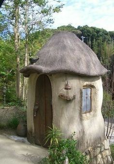 a small house with a thatched roof in the middle of some trees and bushes