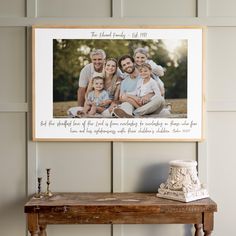 a family photo hanging on the wall next to a table with a vase and candle