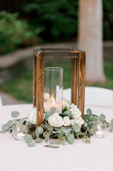 a wooden lantern with flowers and candles on a white table cloth at a wedding reception