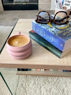 a coffee table with books, glasses and a cup of coffee sitting on top of it