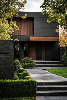 a modern house with black walls and steps leading to the front door is surrounded by greenery