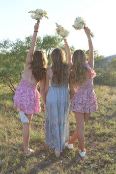 three girls are holding flowers in the air