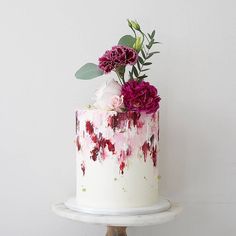 a white cake with red and pink flowers on top is sitting on a wooden stand