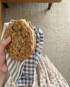 a hand holding a cookie on top of a blue and white checkered cloth next to a wooden table