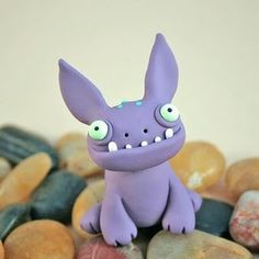 a purple toy sitting on top of some rocks and stones with eyes painted on it