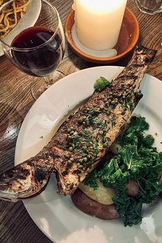 there is a fish and some vegetables on the plate next to a glass of wine