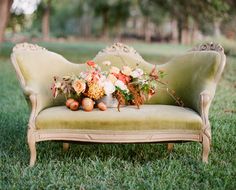 a green couch with flowers and fruit on it in the middle of grass near trees