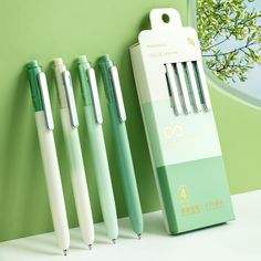 three pens sitting next to each other in front of a green wall with an open box