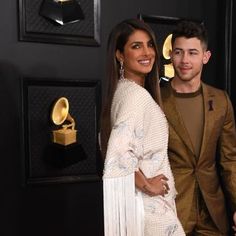 a man and woman standing next to each other on a red carpet with gold jewelry