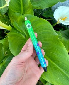 a person holding a green and blue pen in front of some plants with white flowers