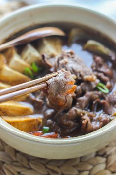 a bowl filled with meat and vegetables on top of a table next to chopsticks