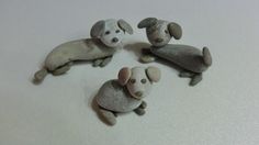 three little dogs made out of rocks on a white surface with one laying down and the other standing up