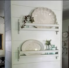 two white shelves with plates and vases on them against the wall in a dining room