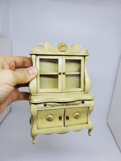 a hand is holding a miniature cabinet with drawers on it's sides and the door open