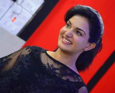 a woman in a black dress smiling at the camera with red wall and electrical equipment behind her