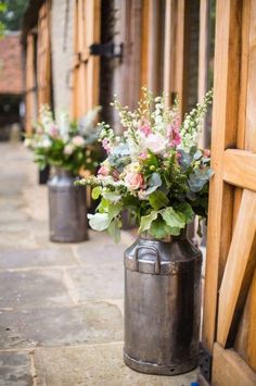 three metal vases with flowers in them sitting on the side of a building next to an open door