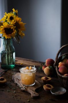 a table topped with a glass filled with liquid next to sliced peaches and a basket of sunflowers