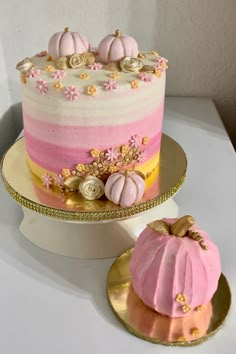 there is a pink and yellow cake on the table next to a plate with two small pumpkins