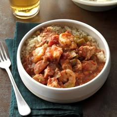 a white bowl filled with shrimp and rice on top of a table next to a glass of beer