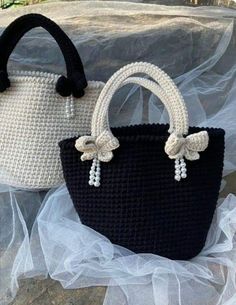 two crocheted purses sitting on top of a white and black table cloth